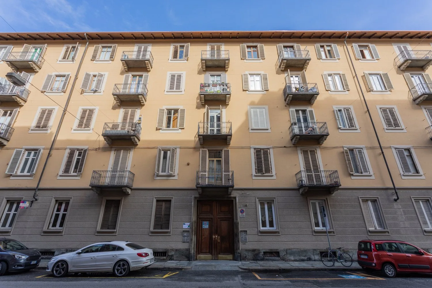 A multi-story residential building with balconies and parked cars along the street.