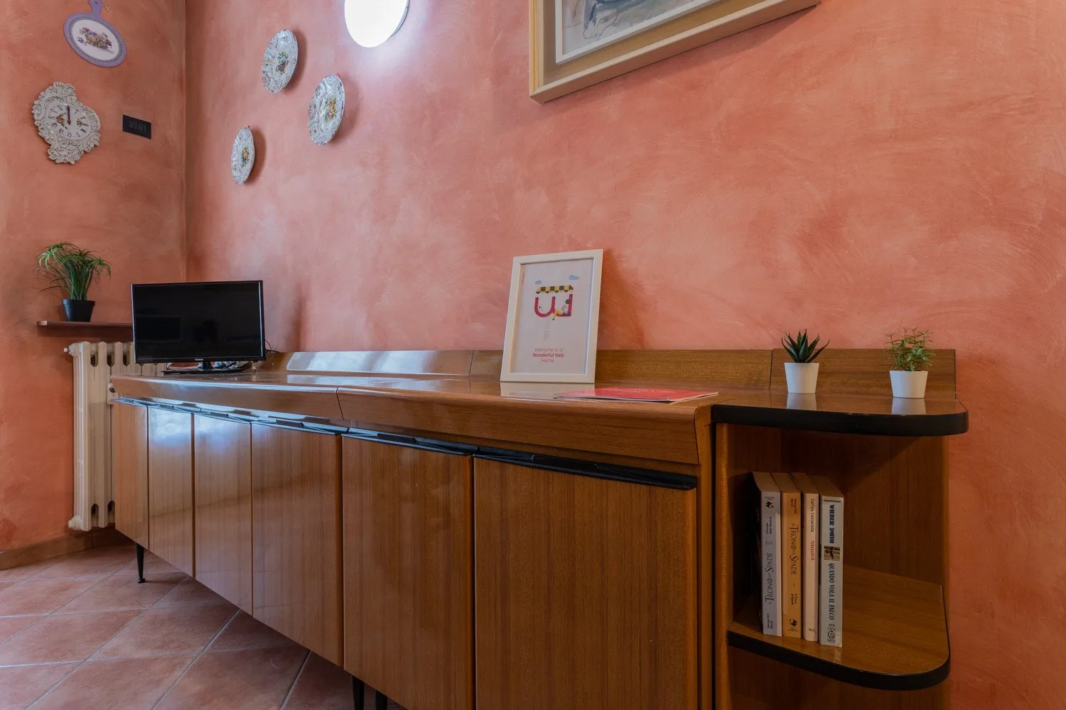 Un mostrador de recepción de madera está junto a paredes color melocotón y un televisor pequeño.