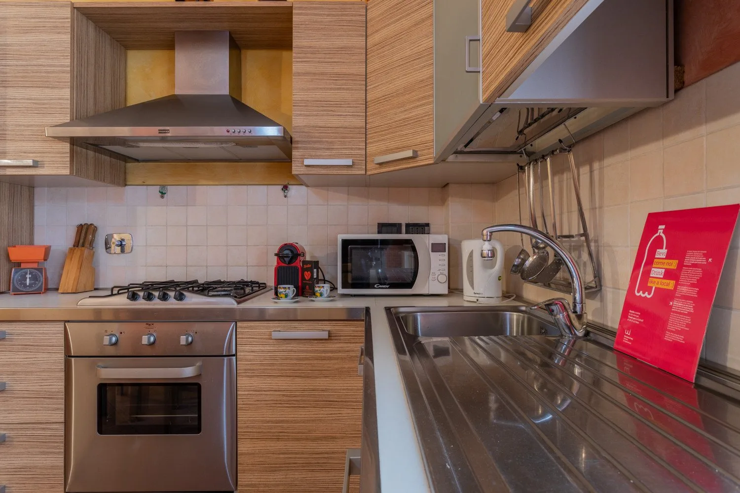 A kitchen with wood cabinets, a stovetop, oven, microwave, and stainless-steel sink.