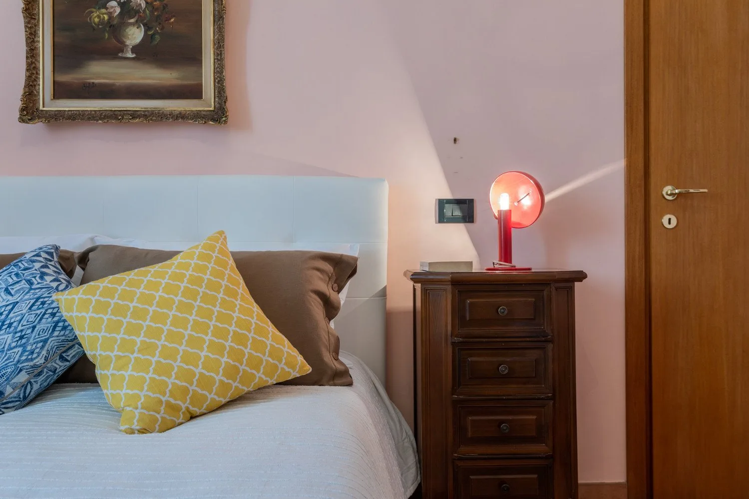 A bedroom with a bed, patterned pillows, and a lit bedside lamp.