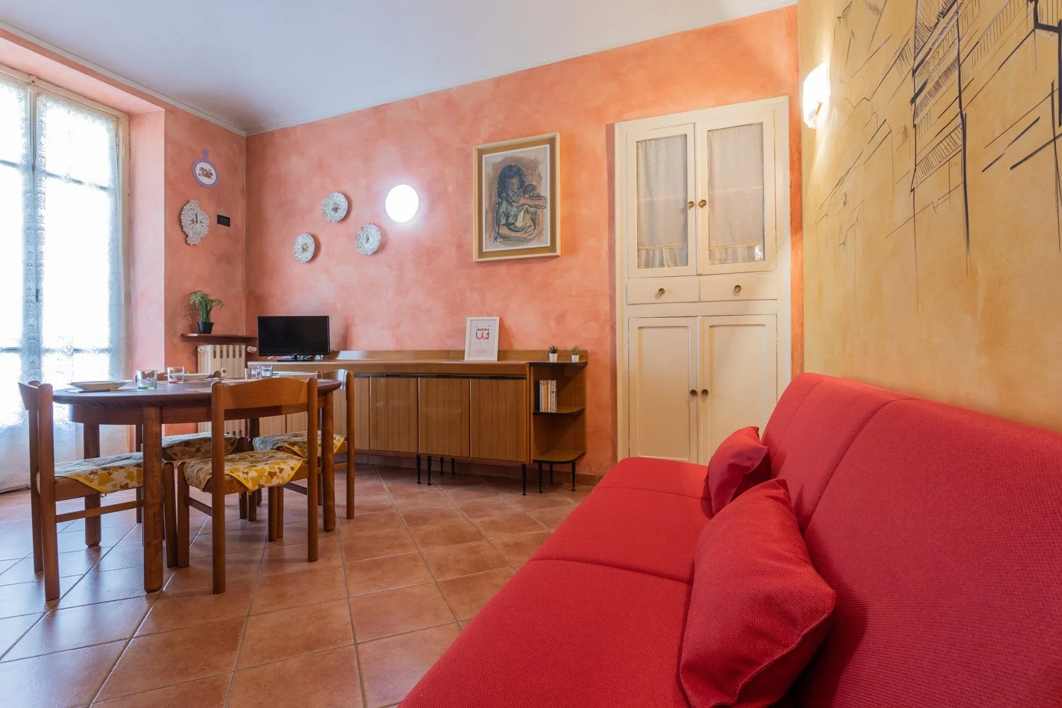 A living and dining area with a red sofa, wooden table, and desk.