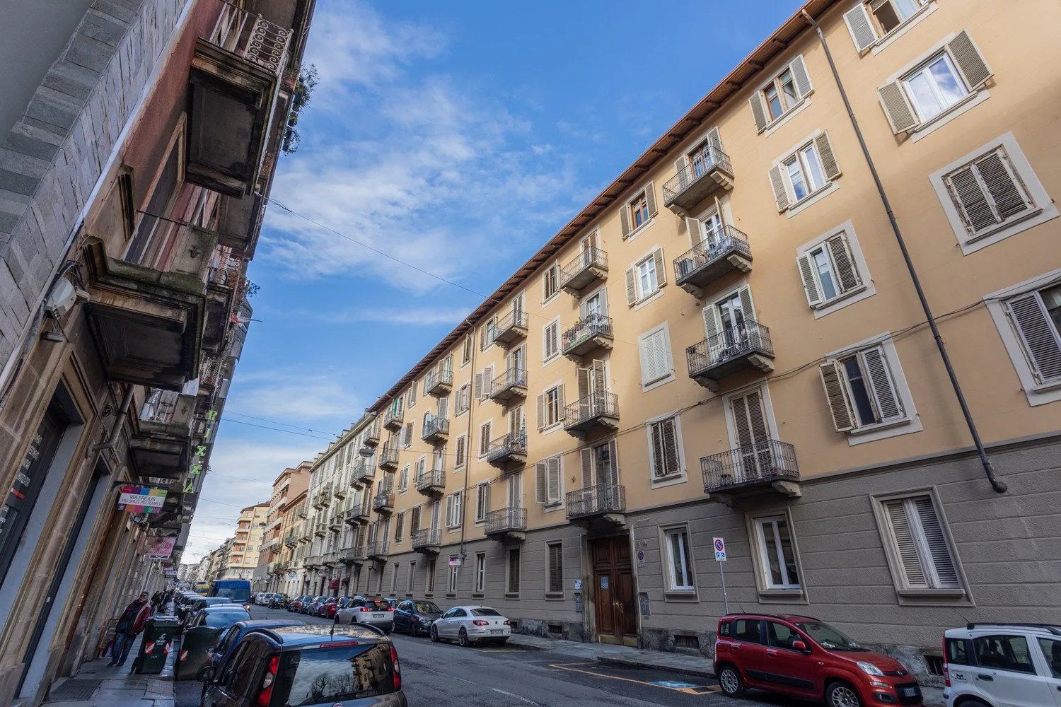 Street scene with a long row of apartment buildings and parked cars.