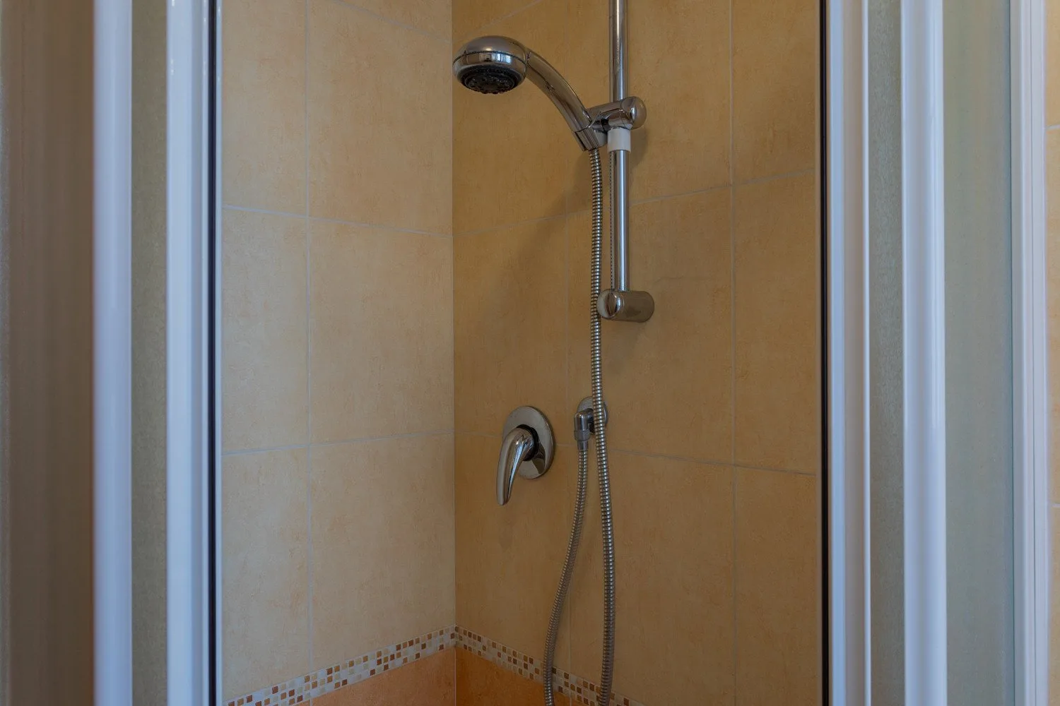 A tiled shower with a handheld showerhead and hose.