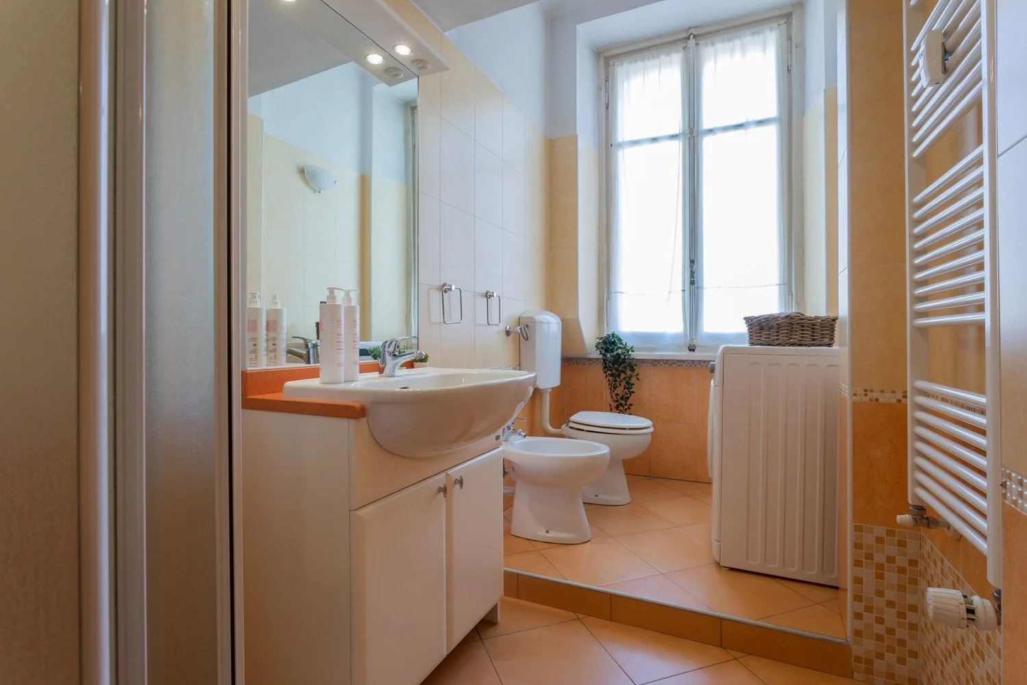 A tiled bathroom with a vanity, toilet, and window.