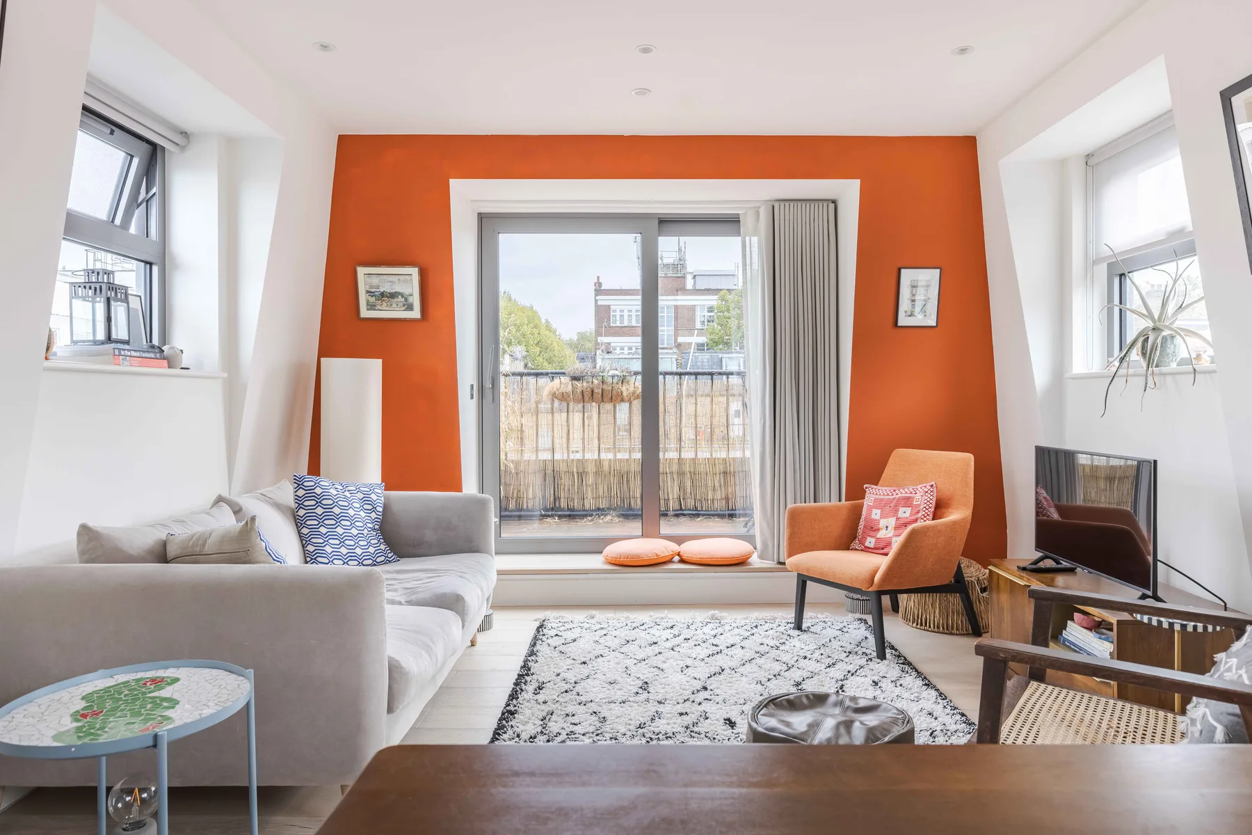 A bright living room with seating, a rug, and glass doors opening onto a balcony.
