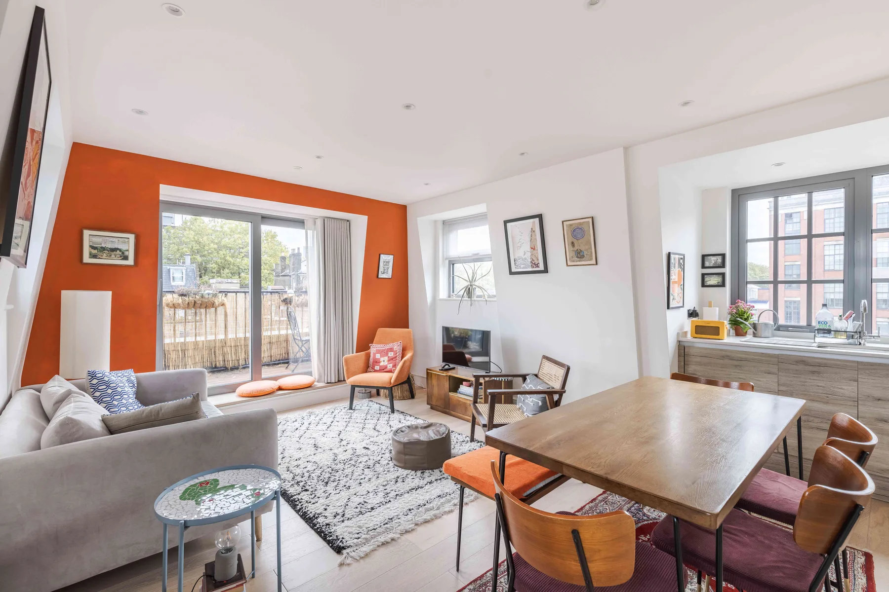 Una luminosa sala de estar y comedor con sofá, mesa grande y pared de acento naranja.