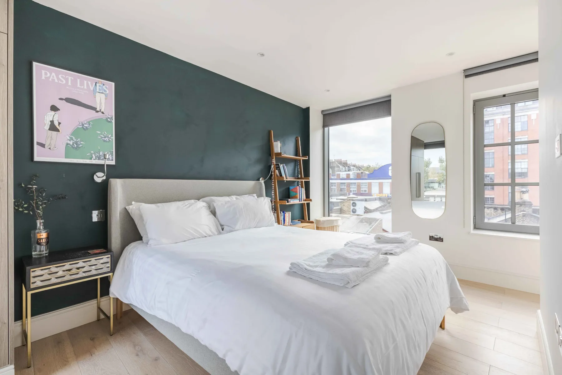A bright bedroom with a large bed and windows overlooking nearby buildings.