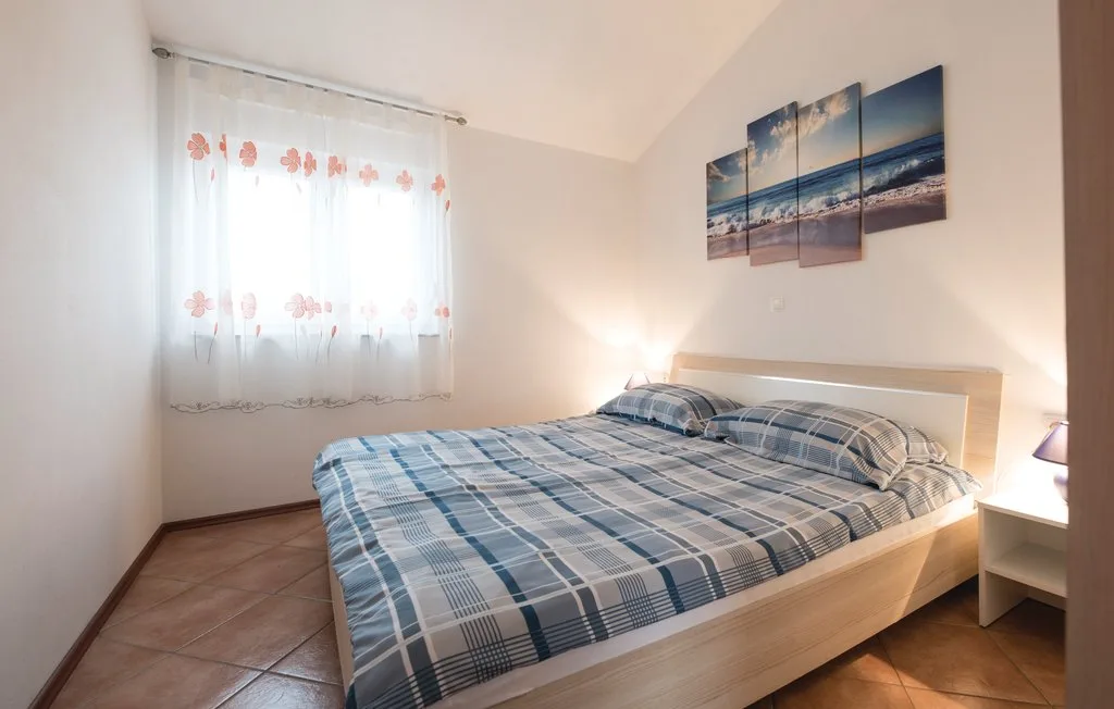 A bedroom with a bed, a curtained window, and beach artwork on the wall.