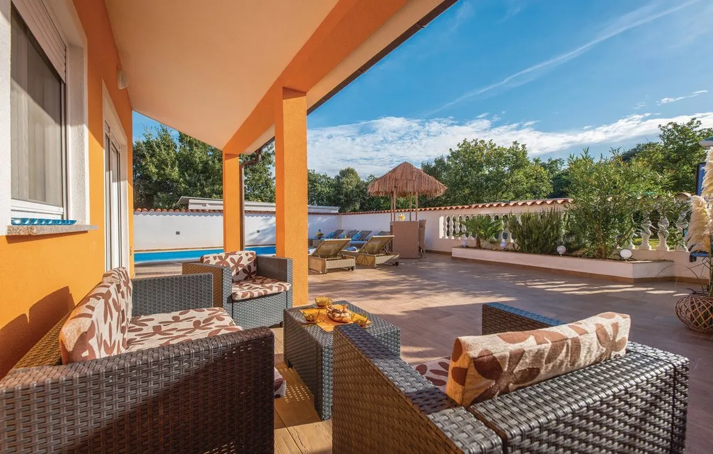 A covered terrace with wicker seating, a small table, and potted plants.