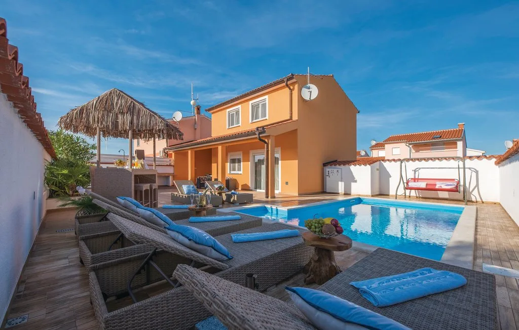 An outdoor pool beside an orange house, with lounge seating and a thatched parasol.