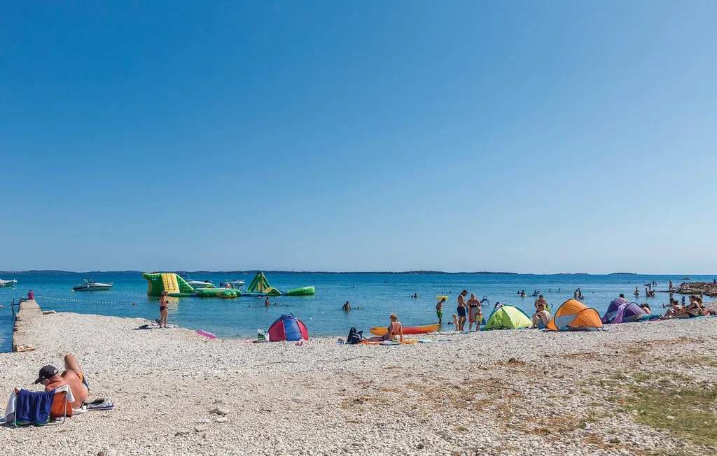 A sandy beach with colorful tents and people beside calm blue water.