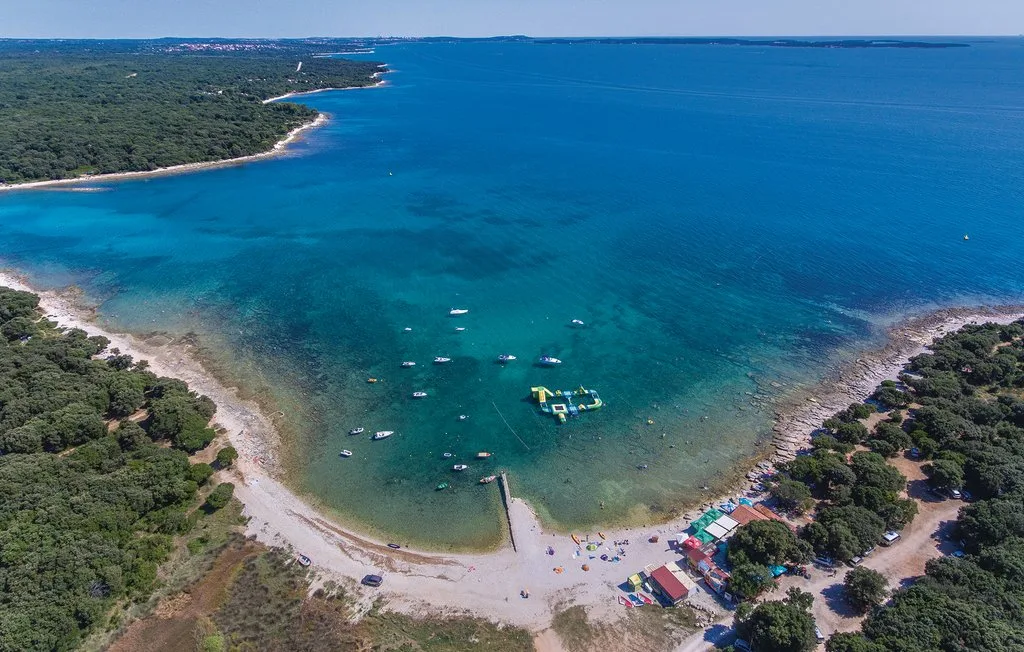 Aerial view of a curved shoreline, turquoise water, and boats near the beach.