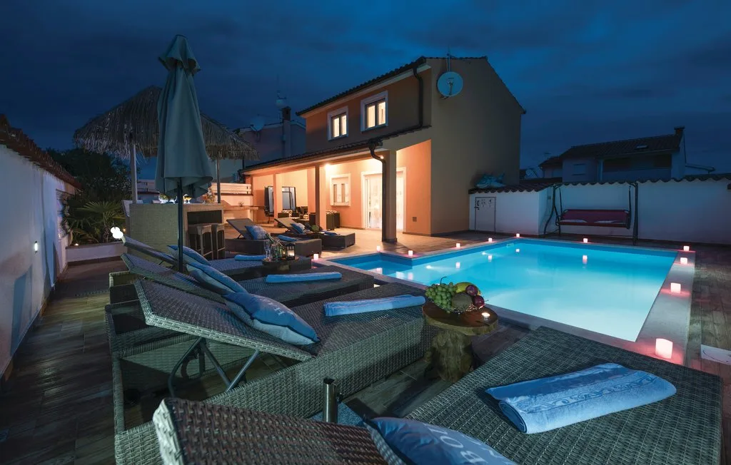 An outdoor pool beside a warmly lit house, with lounge seating on the patio.