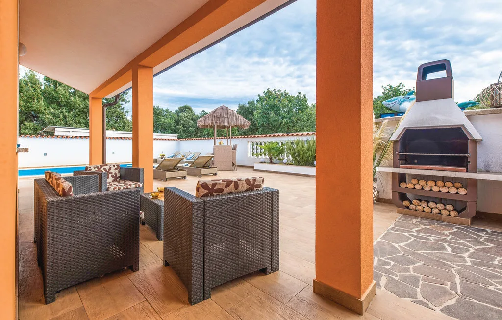 A covered patio seating area overlooks a pool, with an outdoor grill nearby.
