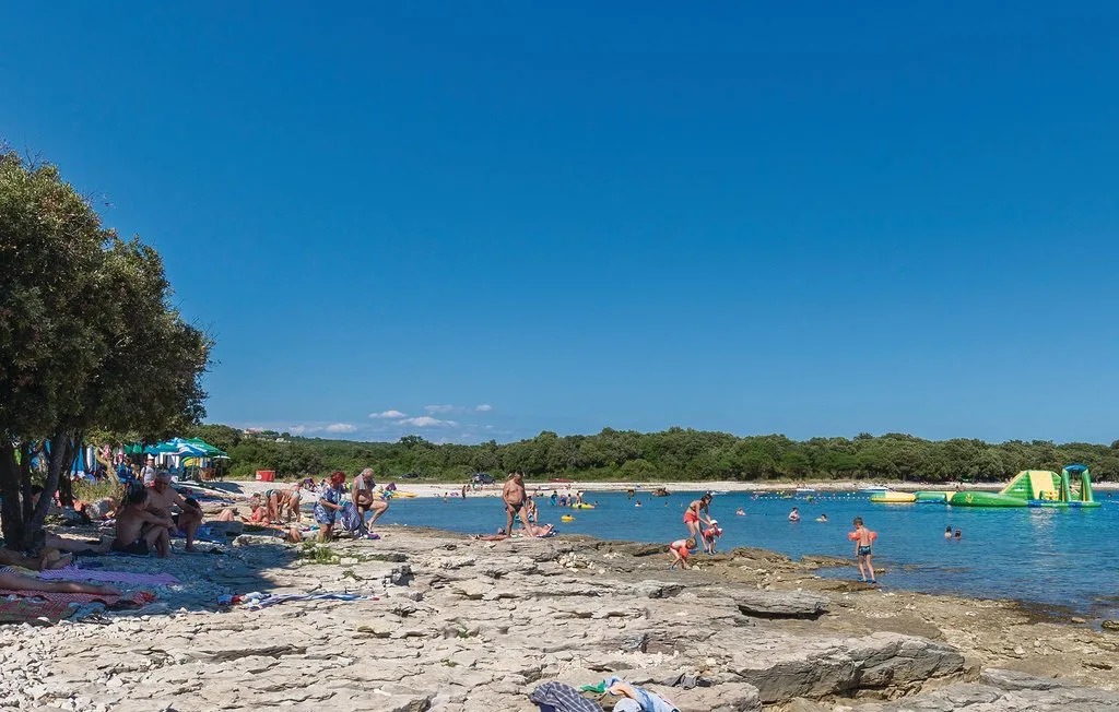 A rocky lakeshore beach with swimmers and colorful umbrellas under a clear sky.