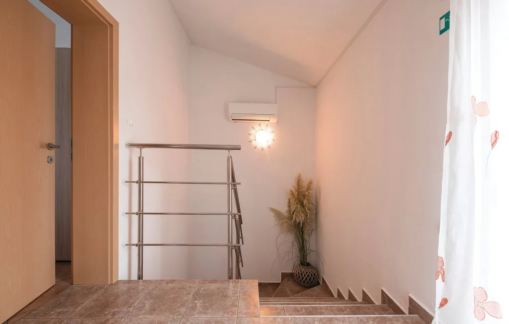 A stair landing with a metal railing, potted plant, and curtained window.