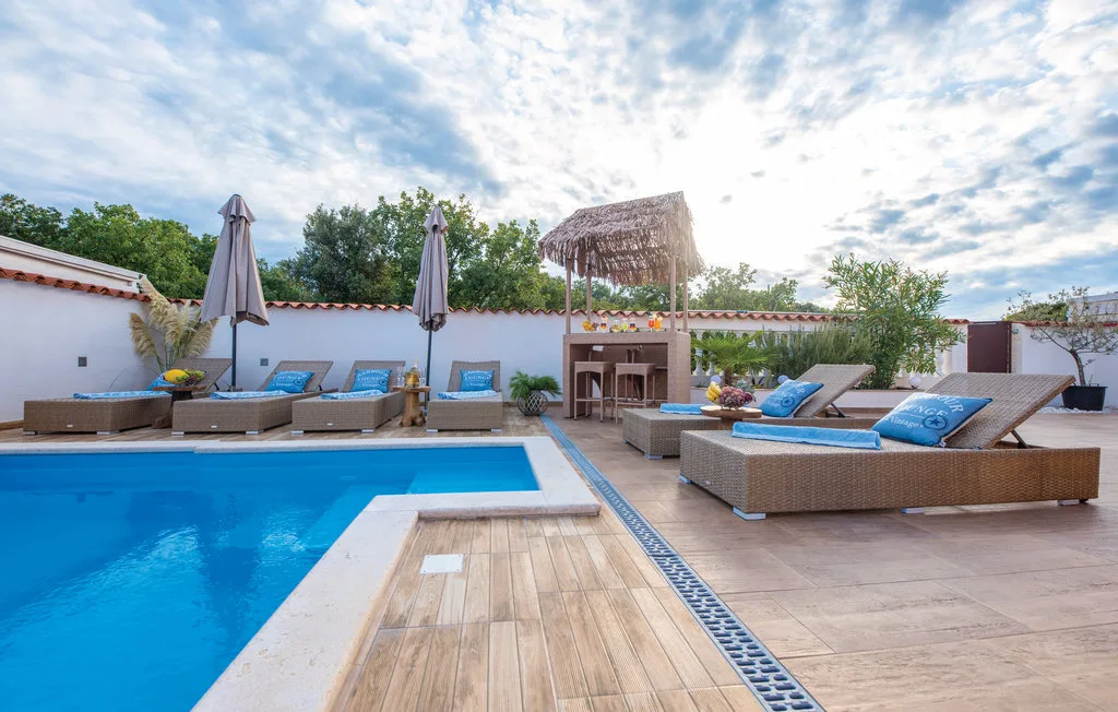 Poolside patio with lounge seating, umbrellas, and a small thatched canopy.