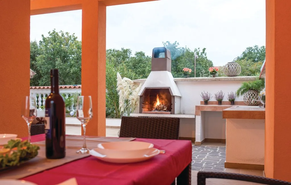 A covered outdoor dining area faces a built-in barbecue with a fire burning.