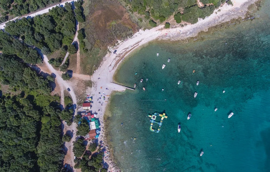 An aerial view of a curved shoreline, with boats floating in clear water.