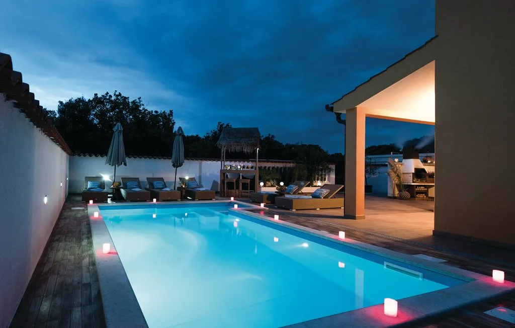 A lit swimming pool beside a covered patio at dusk.