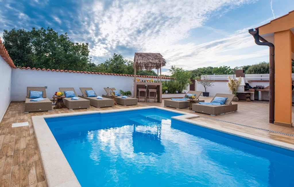 Una piscina al aire libre está rodeada de asientos y un bar con sombra.