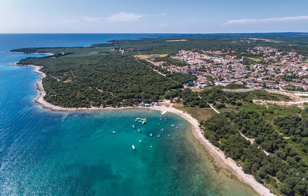 Aerial coastal landscape with a forested shoreline and boats in turquoise water.