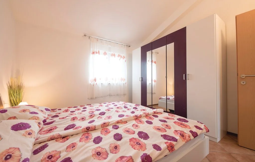 A bedroom with a double bed covered in floral bedding and a mirrored wardrobe.