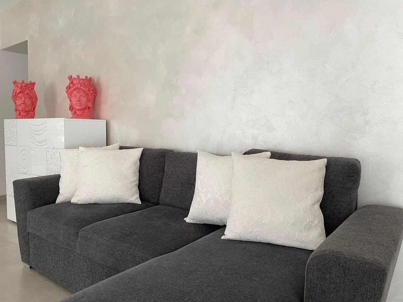 A dark gray sectional seating area with white cushions and red decorative busts.