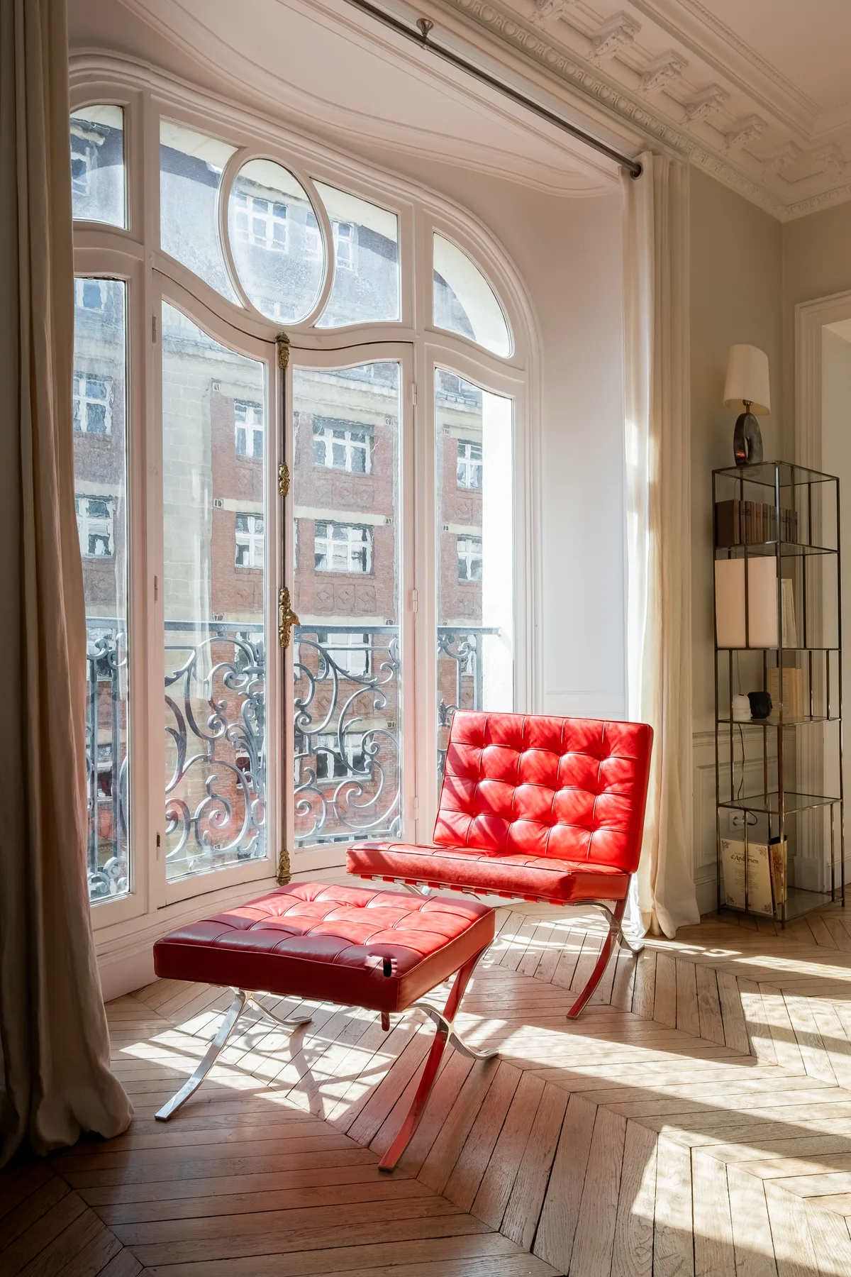 A bright sitting area with a red lounge chair beside tall arched windows.