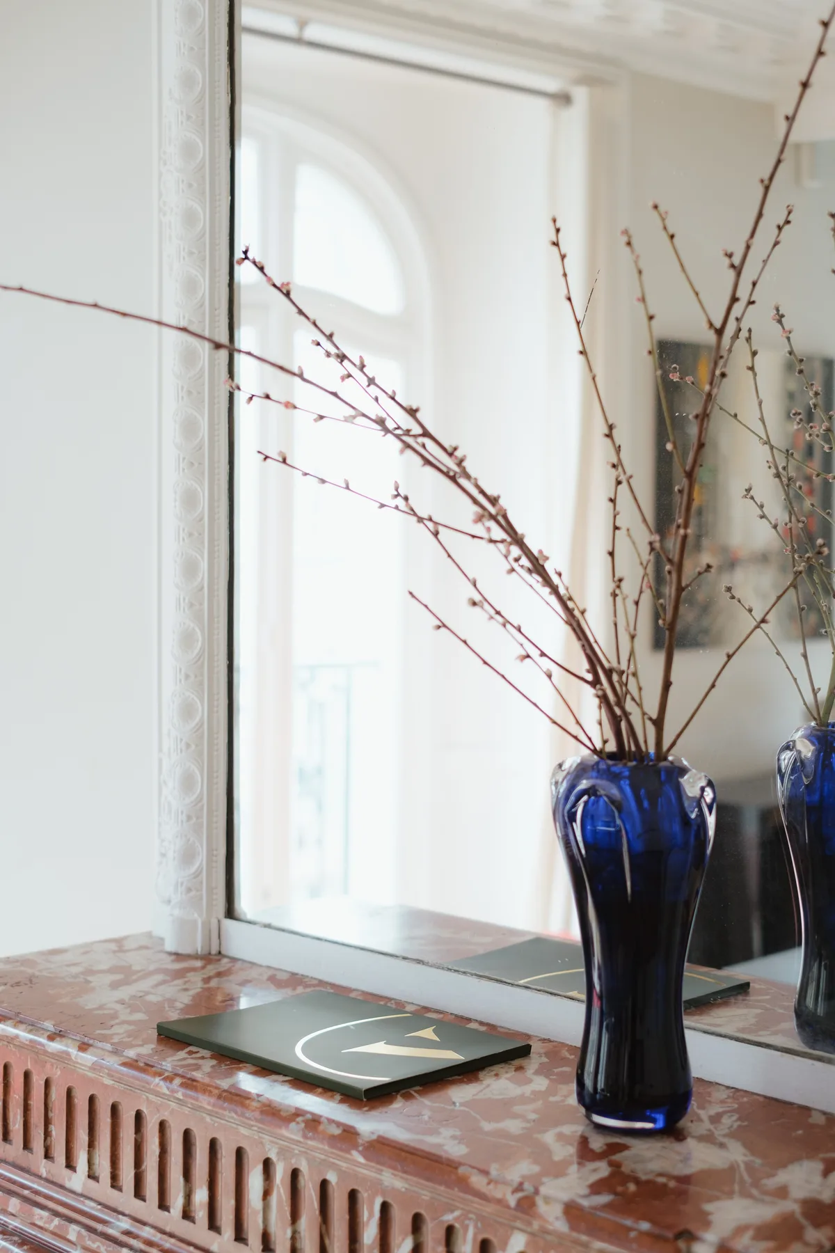 A bright interior with a blue vase of branches on a windowsill.