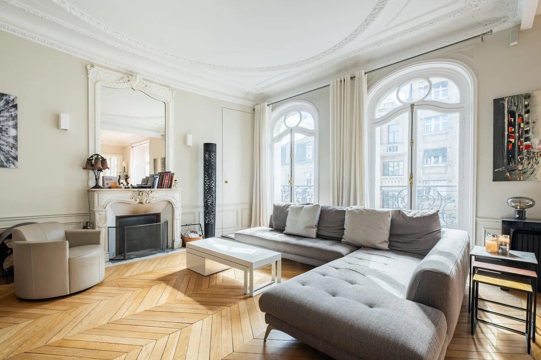 Una sala luminosa con sofá seccional gris, chimenea y ventanas altas con arco.