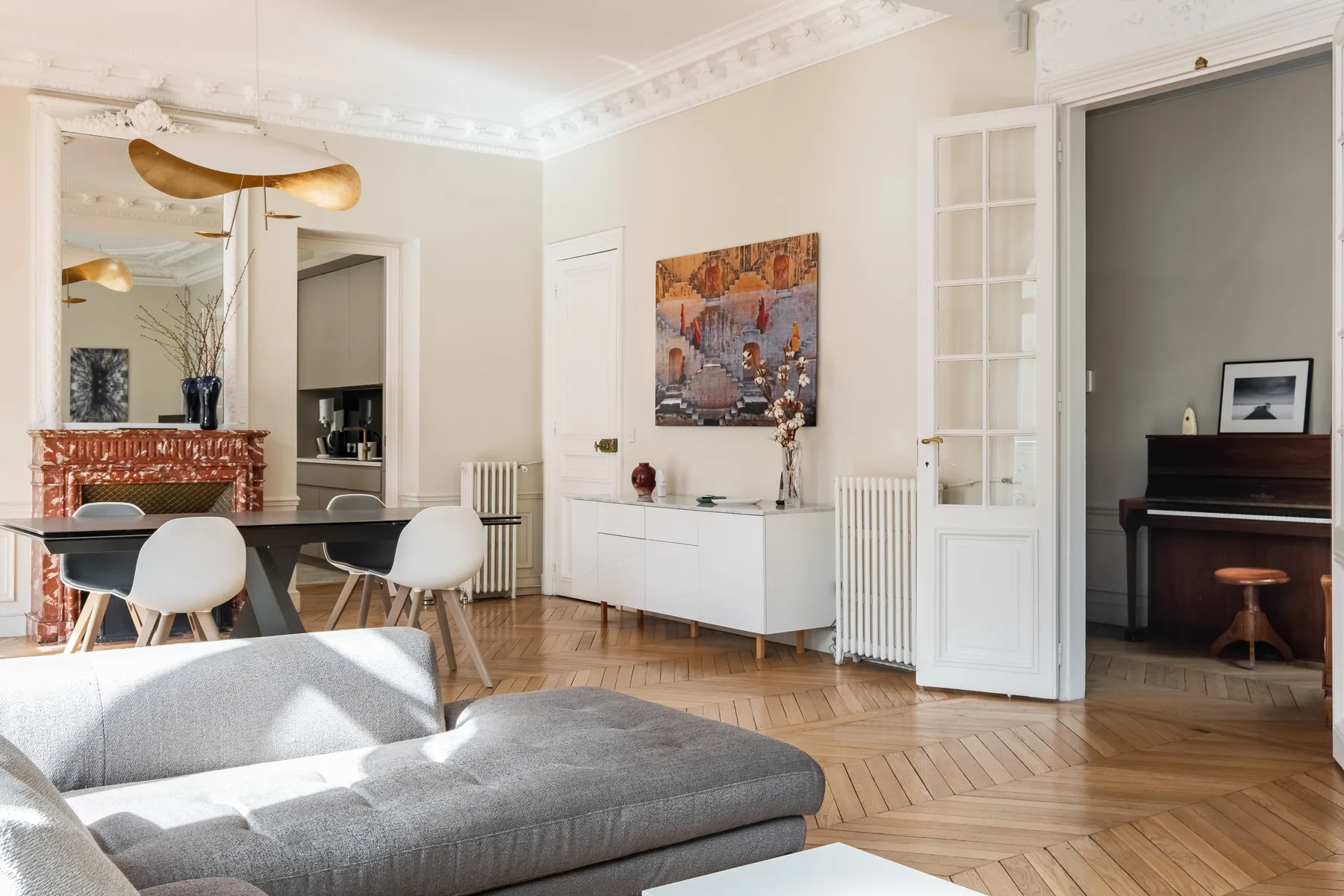 Una sala luminosa con mesa de comedor, asientos grises y un piano en una habitación contigua.