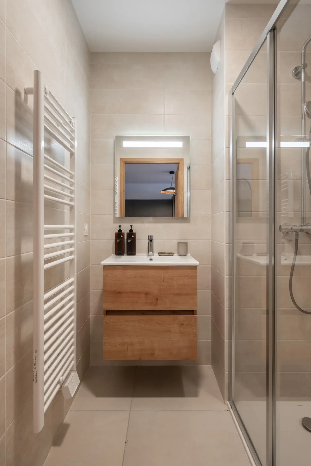 Modern bathroom with wooden vanity, large mirror, glass shower enclosure, and white heated towel rail, in a neutral-toned decor.