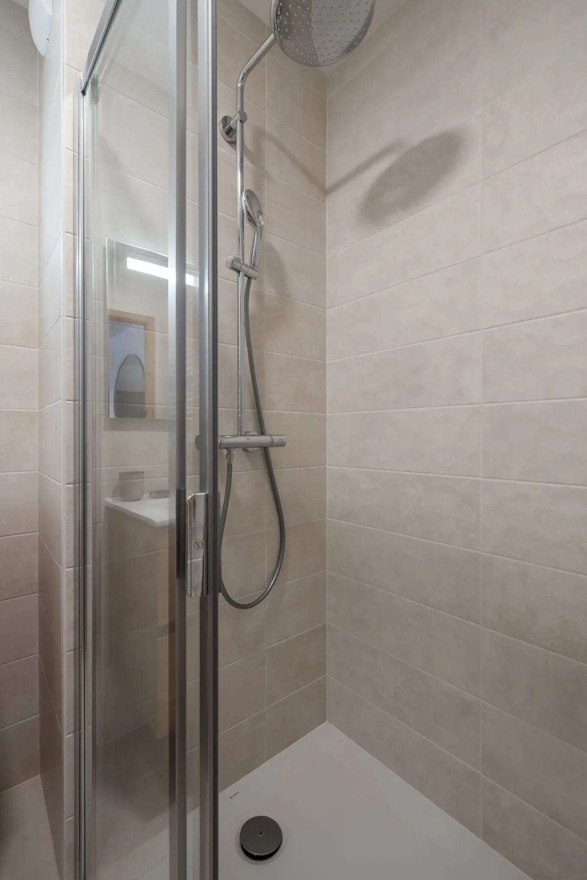 Modern bathroom with wooden vanity, large mirror, glass shower enclosure, and white heated towel rail, in a neutral-toned decor.