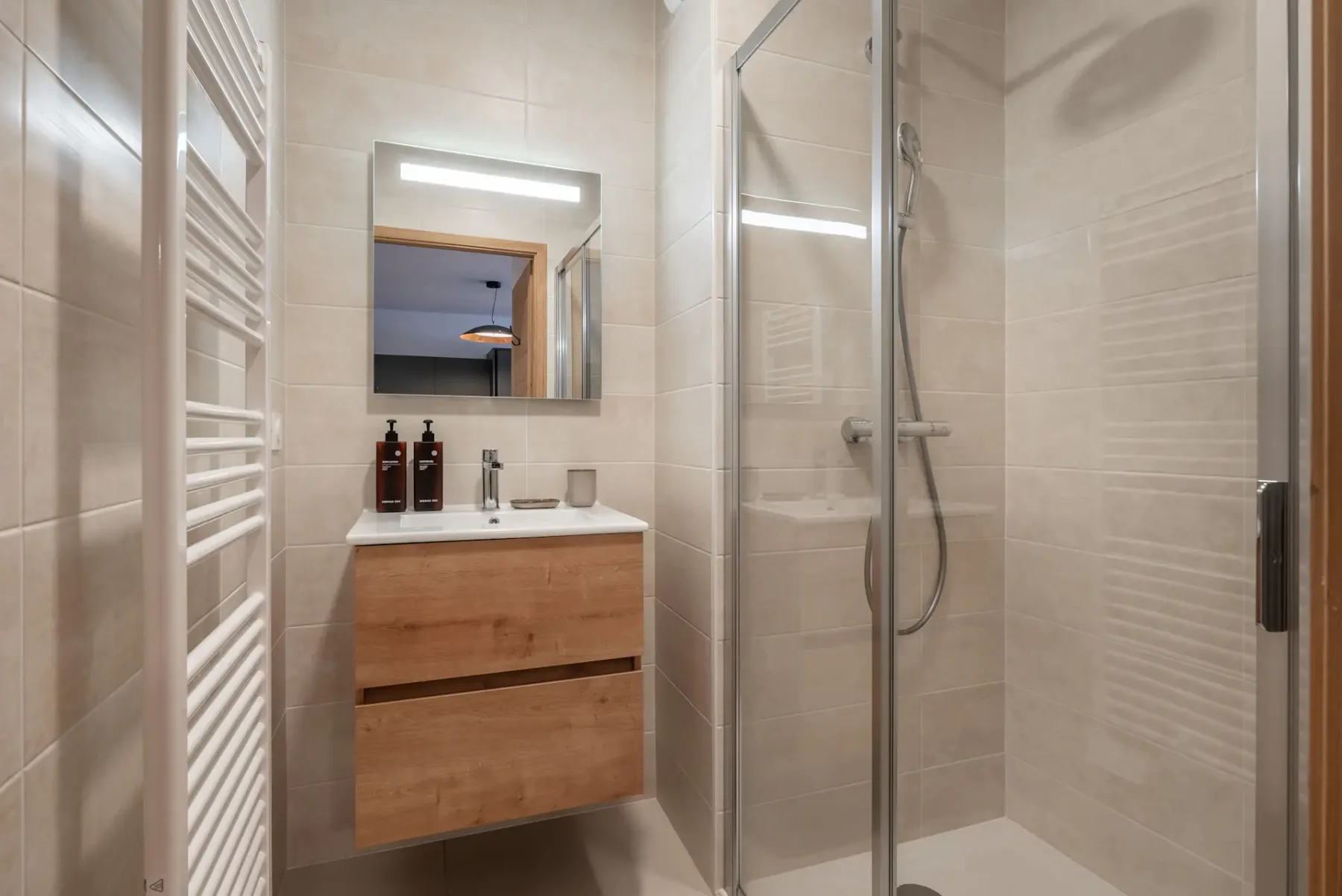 Modern bathroom with wooden vanity, large mirror, glass shower enclosure, and white heated towel rail, in a neutral-toned decor.