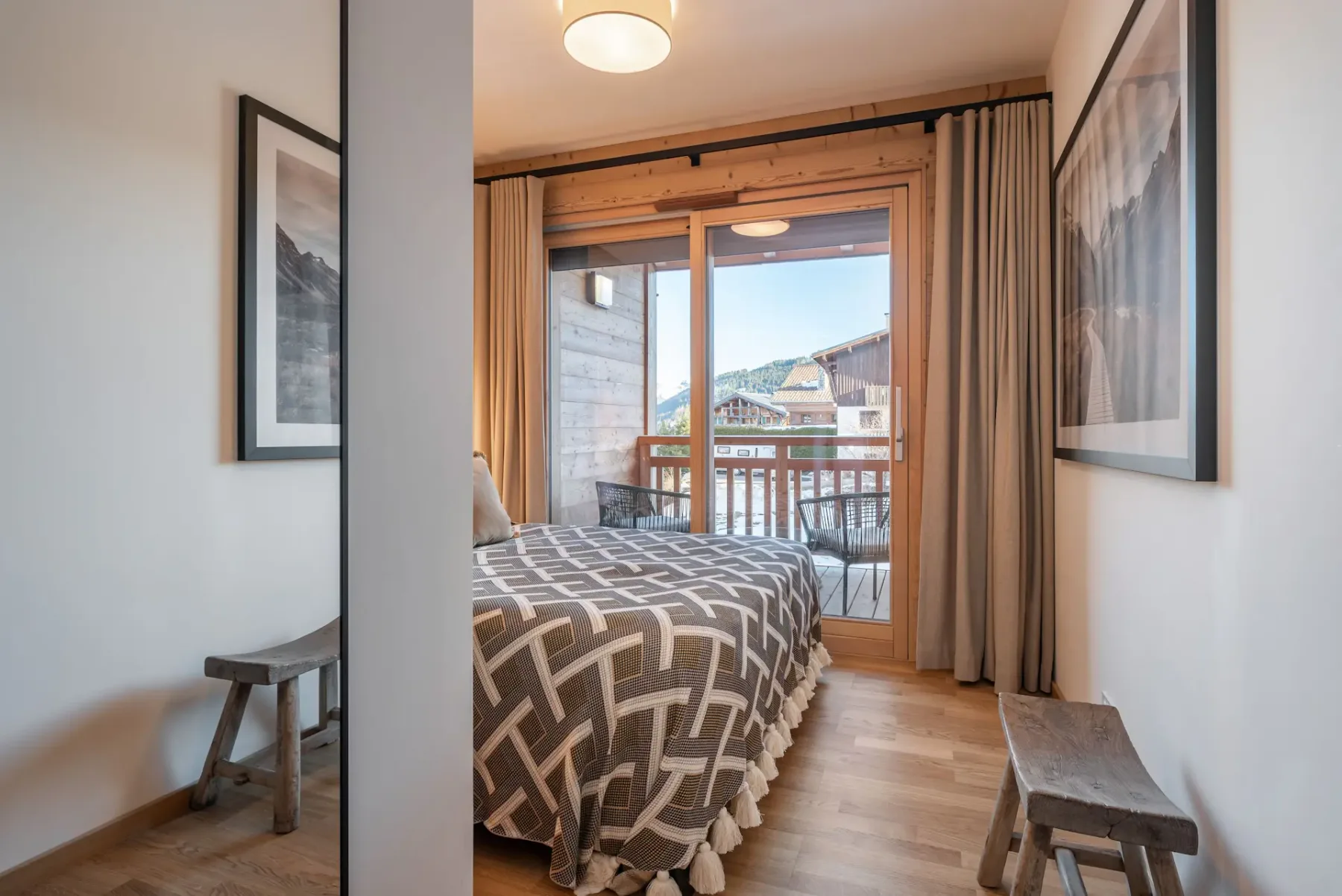 Cozy bedroom with wooden walls, a double bed, and a geometric bedspread. Glass doors open to a balcony with mountain views.