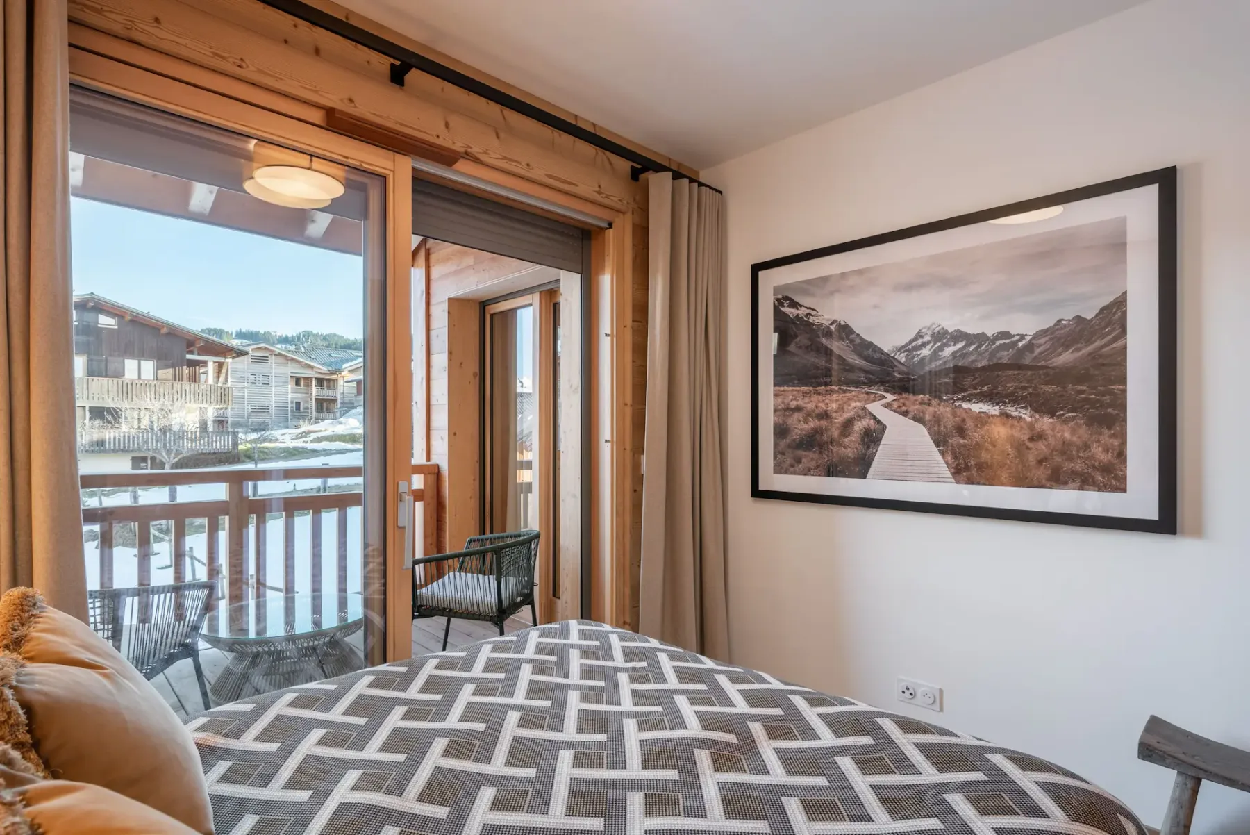 Cozy bedroom with wooden walls, a double bed, and a geometric bedspread. Glass doors open to a balcony with mountain views.