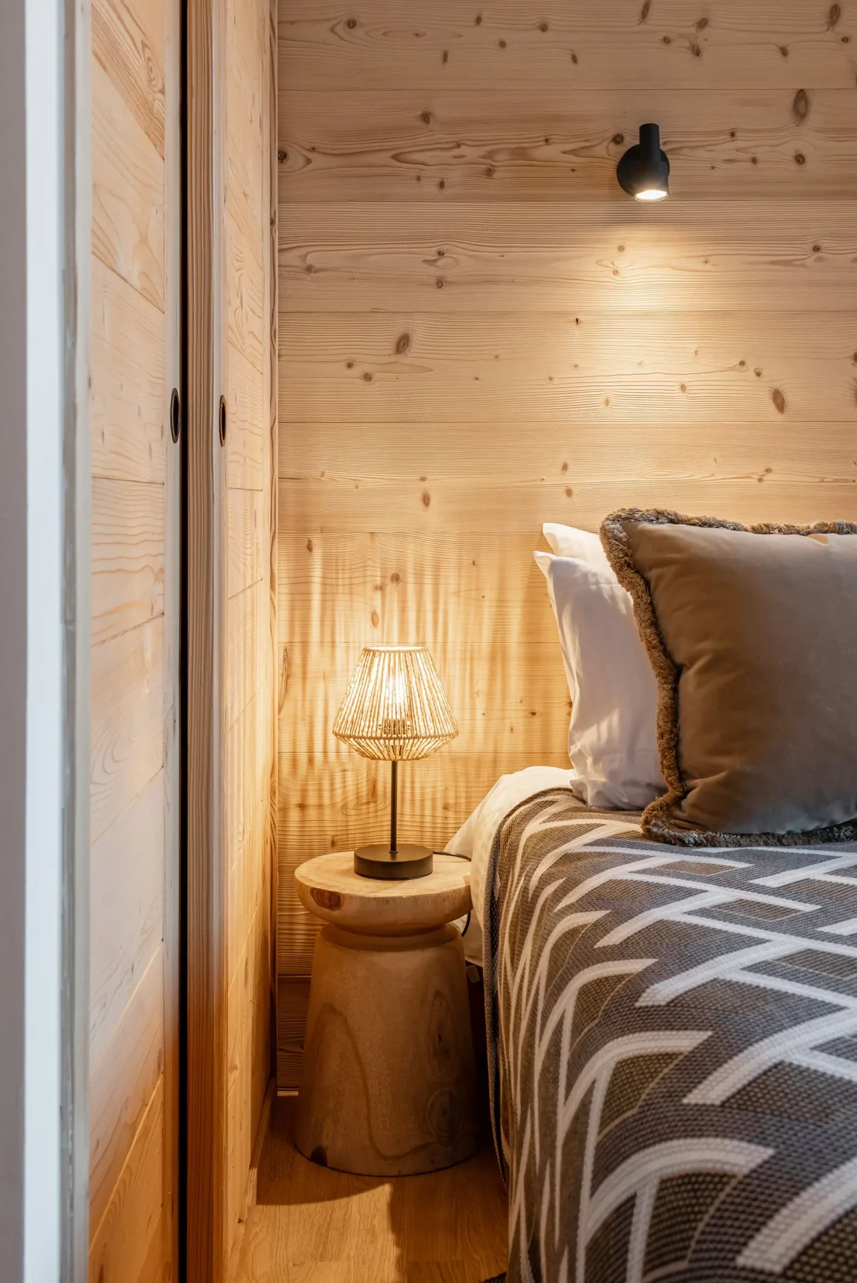 Cozy bedroom with wooden walls, a double bed, and a geometric bedspread. Glass doors open to a balcony with mountain views.