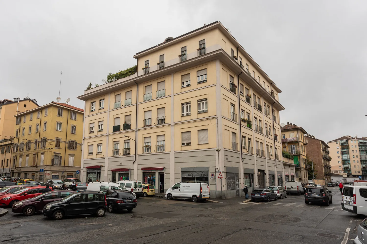 Un edificio beige de varias plantas con filas de ventanas se alza junto a una calle urbana.