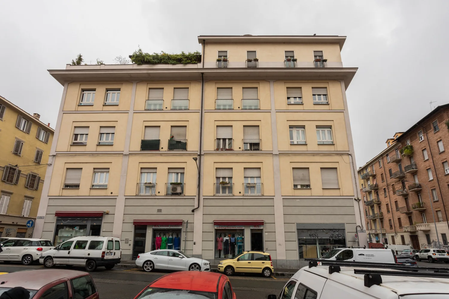Un edificio urbano de varias plantas con filas de ventanas da a una calle con coches estacionados.