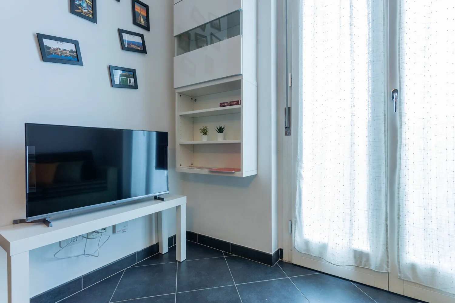 Una sala luminosa con televisor, estantes de pared y cortinas translúcidas.