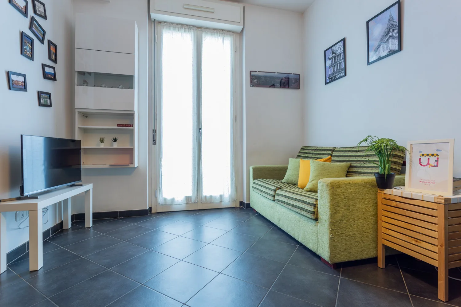 Una sala de estar con sofá verde, televisor y una ventana luminosa.