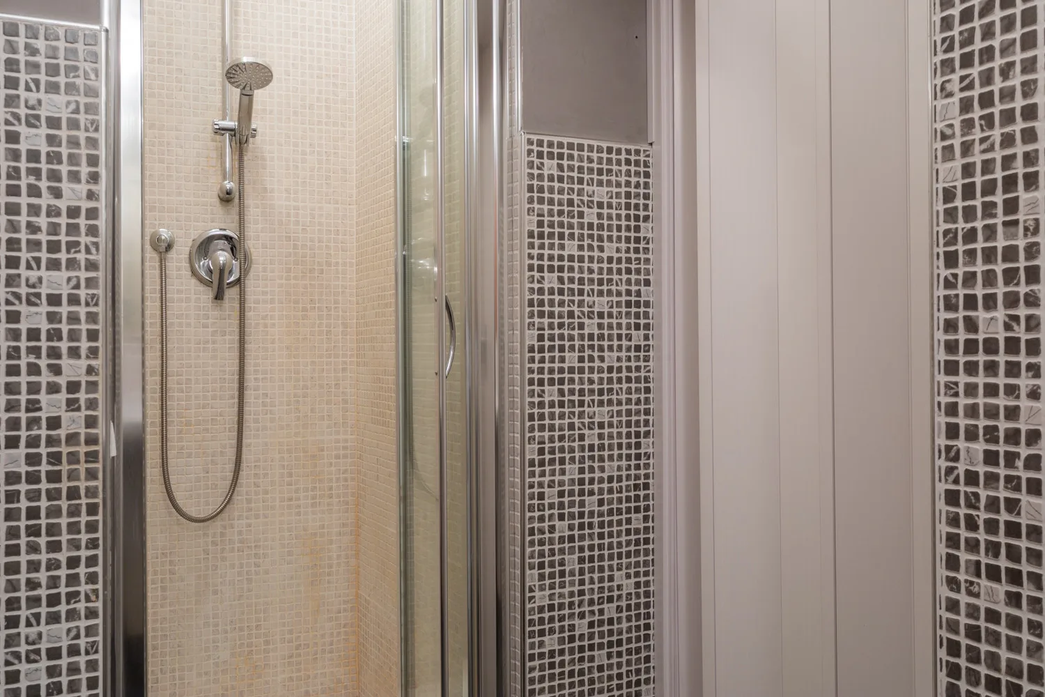 Una ducha de baño con azulejos, cabezal de mano y paneles de vidrio.