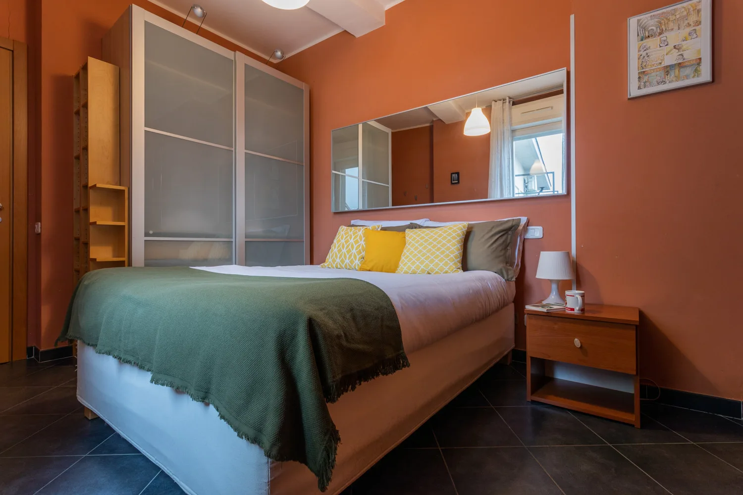 Un dormitorio con una cama, cojines de colores y un espejo en la pared.