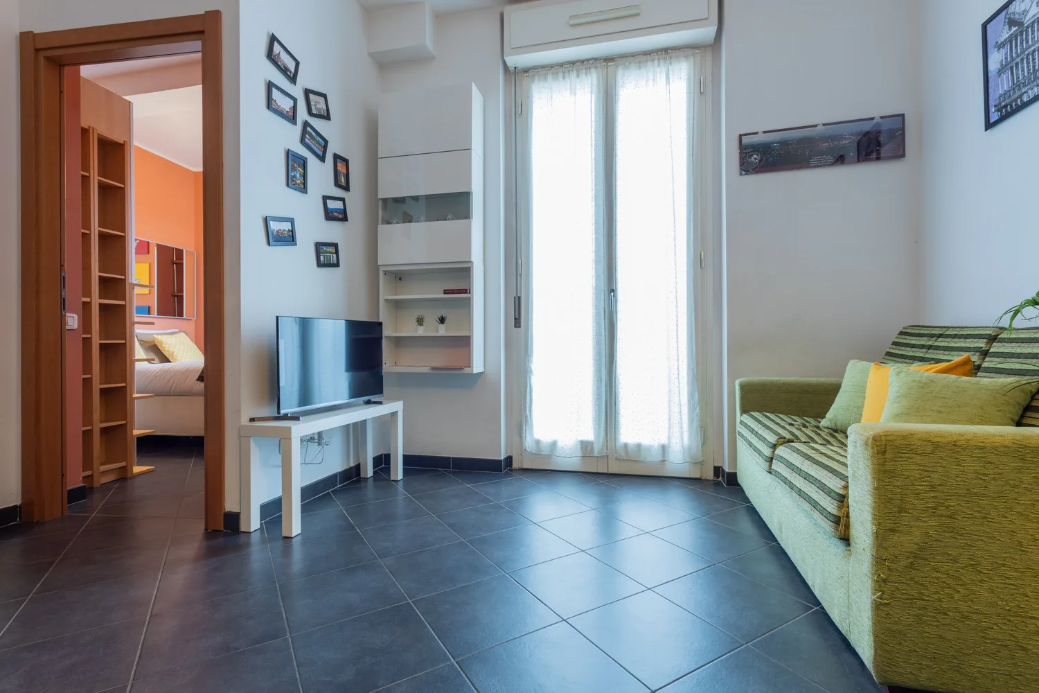 Una sala de estar con televisor, asientos y una puerta de vidrio luminosa.
