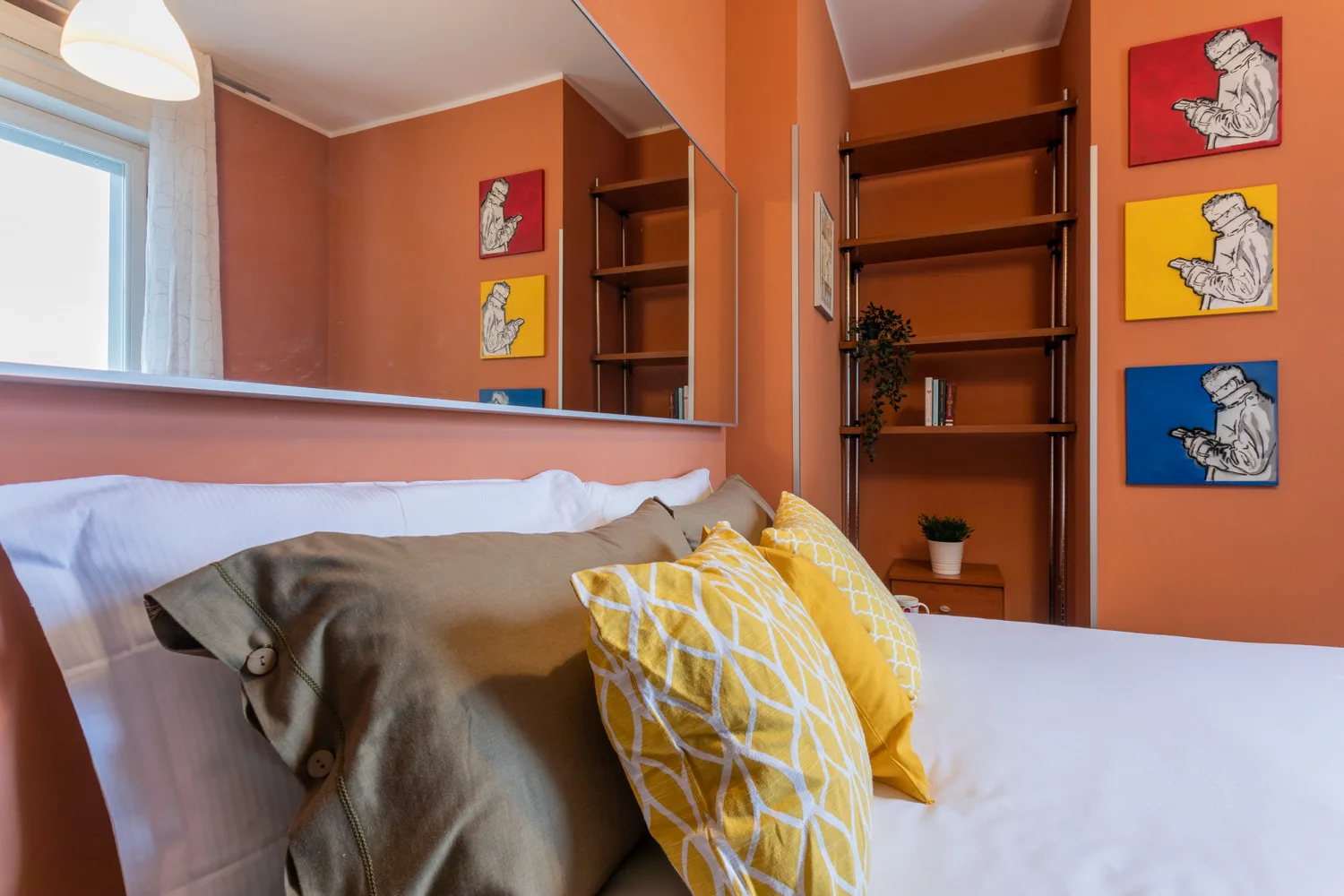 Un dormitorio con una cama y cojines coloridos junto a una estantería empotrada.