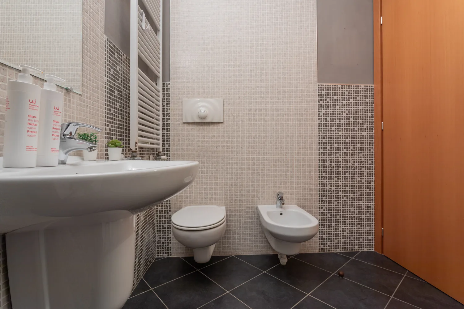 Un baño alicatado con lavabo, inodoro, bidé y puerta de madera.