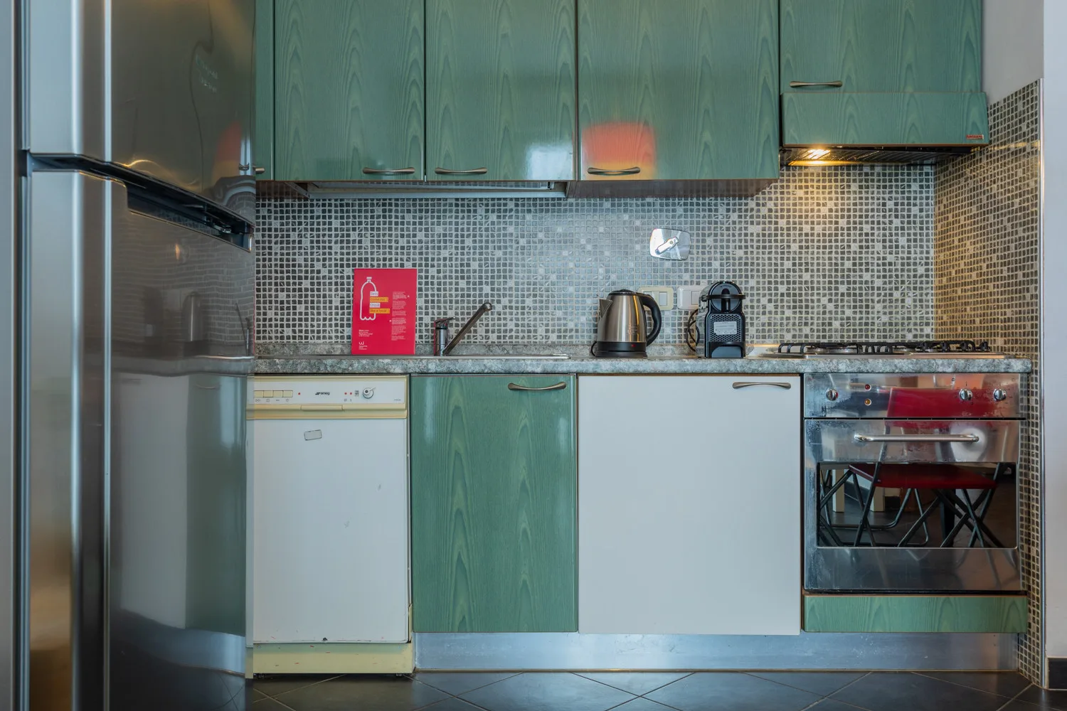 Una cocina compacta con gabinetes verdes, un refrigerador y un salpicadero de azulejos.