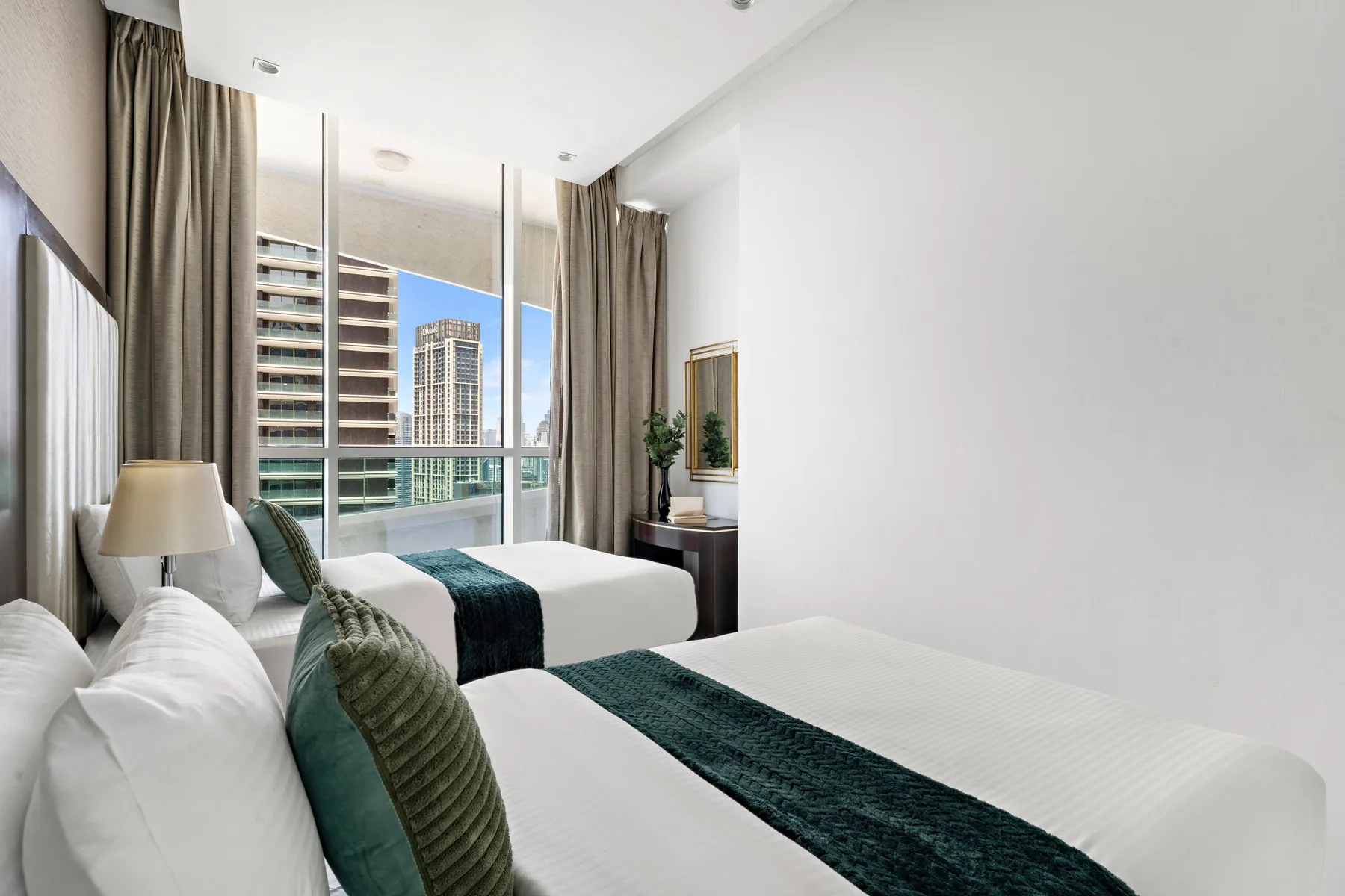 Un dormitorio luminoso con dos camas frente a una gran ventana y vistas de la ciudad.