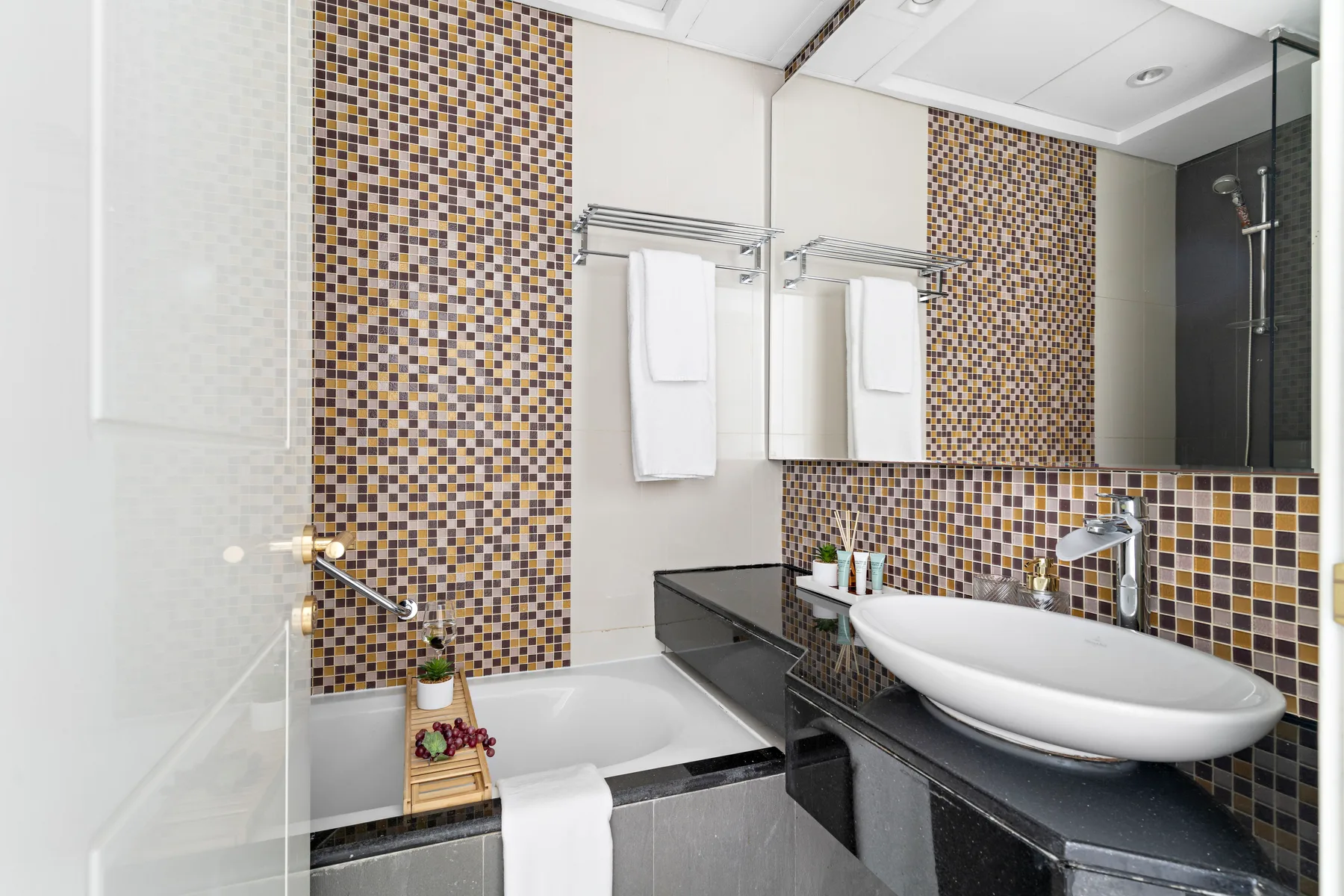 Un baño moderno con bañera, lavabo sobre encimera y paredes de mosaico.